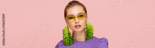 young woman in colored eyeglasses and fresh lettuce earring isolated on pink, banner