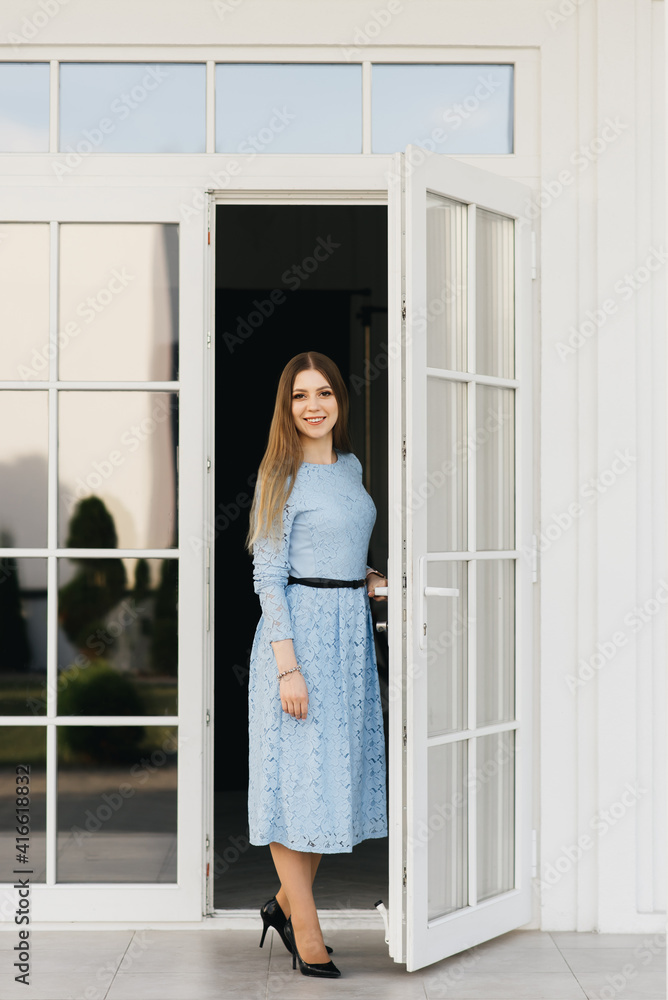 Attractive young girl on the background of the white house in a blue dress Attractive young girl on the background of the white house in a blue dress