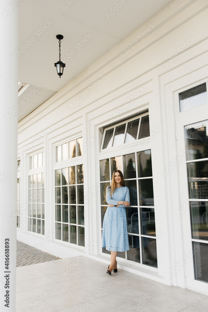 Attractive young girl on the background of the white house in a blue dress