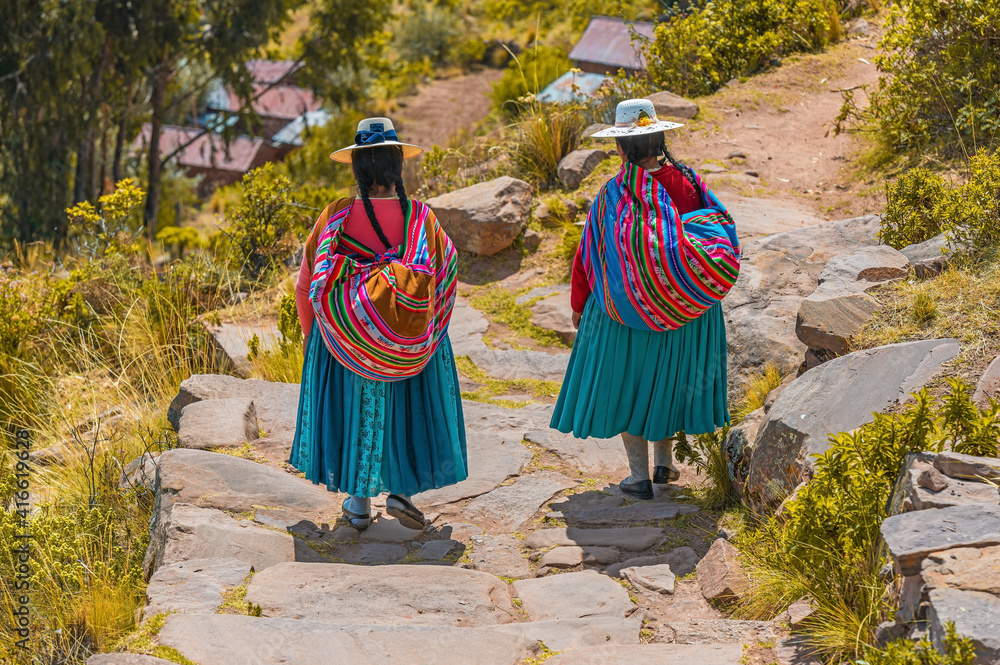 Fototapeta Two Peruvian indigenous Quechua women walking along a trail in traditional clothing and textile bag, Taquile Island, Peru.