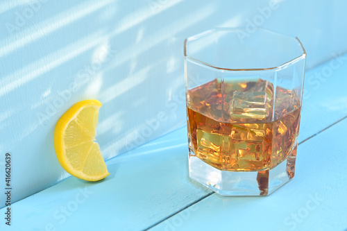 Glass of whiskey with ice and lemon on a blue rustic wooden background