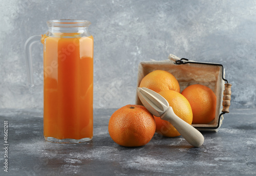 Jug of juice and basket of oranges on marble background