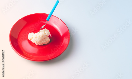 Piece of cauliflower pricked with a small fork on a red plate on white background.