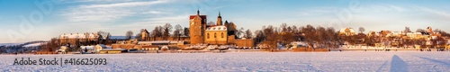 Wunderschönes breites Panorama eines zugefrorenen See mit traumhaften Schloss und winterlicher Natur photo