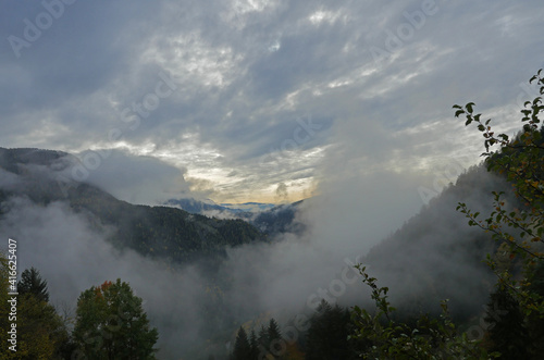 Majestic view of high mountains covered by clouds. Northern lands under an inspiring sunset behind the clouds. Landscape of forests and rocky mountains in north italy.