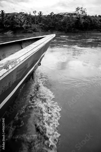 Boat, canoe, raft on the Huallaga River in the Peruvian high jungle. River among vegetation with light blue sky and white clouds.
