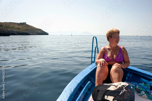 Blond woman sitting in a rowboat heading toward the coast. Cruising.