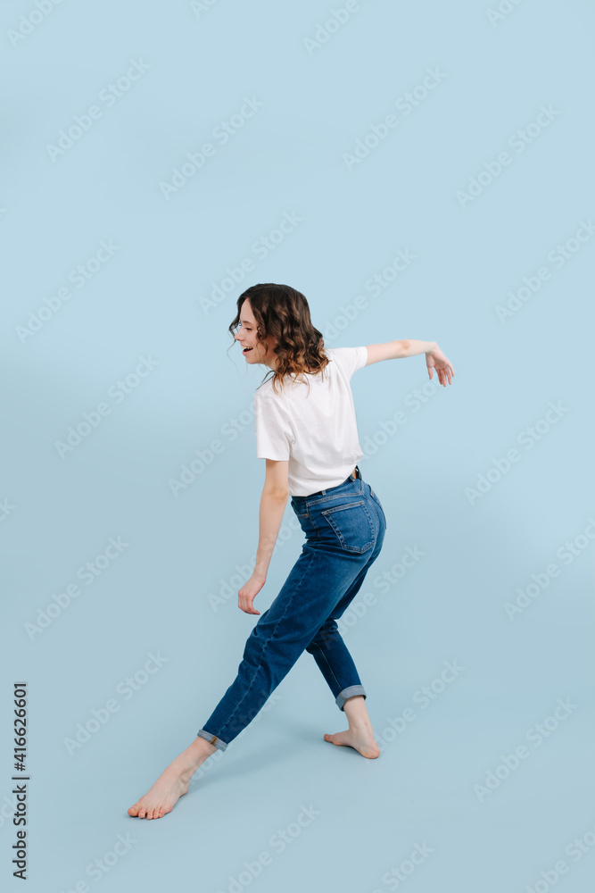 Carefree contemporary dancer poses in front of blue studio background. She's has one straight leg put forward, and other bent in a knee. Her back is straight. Carefree contemporary dancer poses in front of blue studio background. She's has one straight leg put forward, and other bent in a knee. Her back is straight.