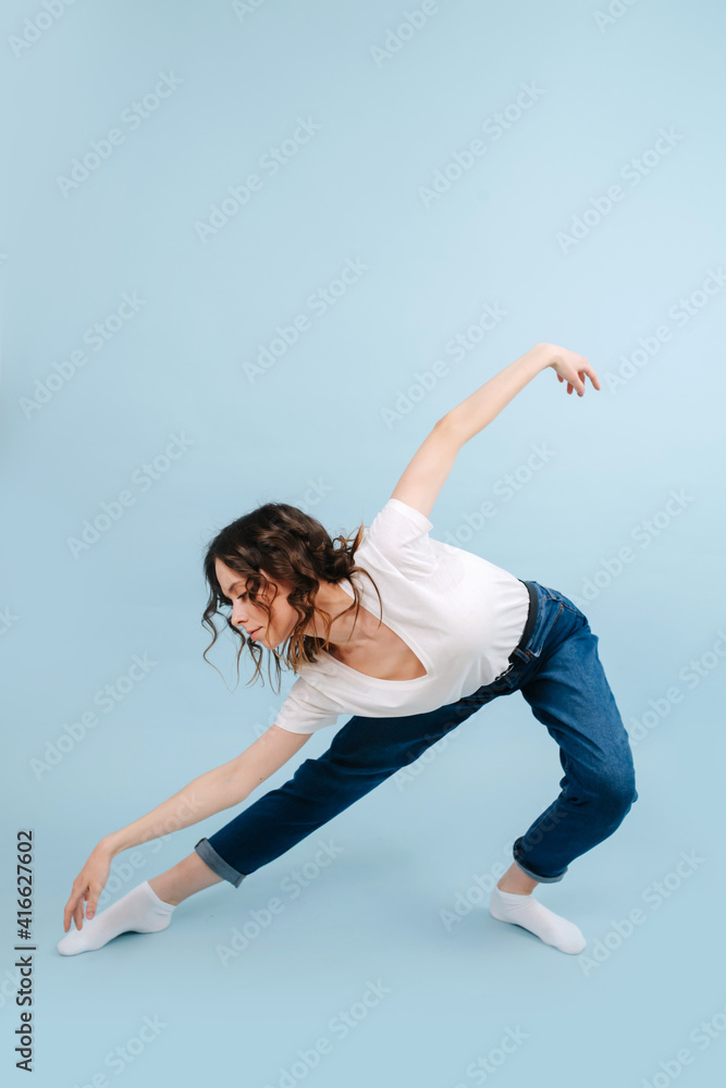 Graceful contemporary dancer poses in front of blue studio background. She's making deep artistic bow with straight leg put forward.