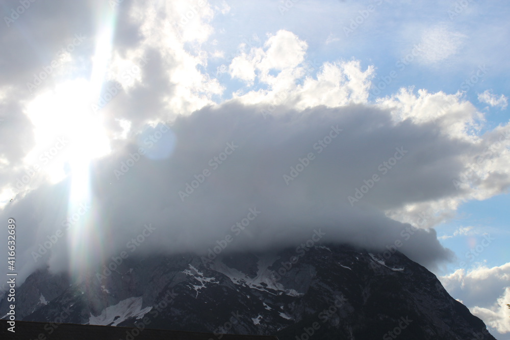 weiße Wolken, Himmel und Sonne über einem Berg in der Steiermark in Österreich