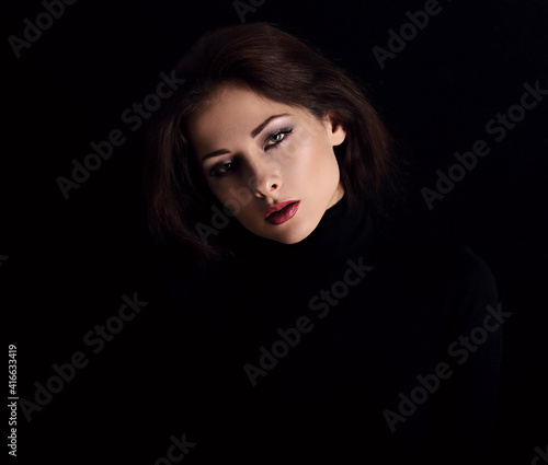 Sexy strong look woman with smirking smiling posing isolated on dark shadow black background. Closeup portrait in deep low key light shadows.