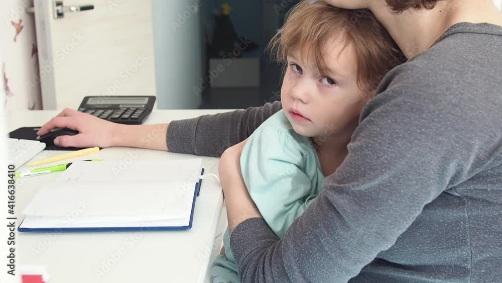 Sad cryed child girl sits in mothers lap while she works online from home. Candid authentic and real life mom working and parenting. Home office Sad cryed child girl sits in mothers lap while she works online from home. Candid authentic and real life mom working and parenting. Home office