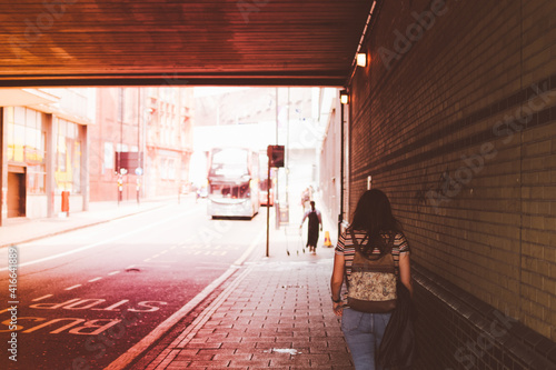 Young woman on her back wearing jeans with a backpack walking through a tunnel, next to a bus stop in Birmingham, United Kingdom