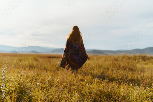 wrapped in plaid figure of a girl with long hair spread on her back is removed along the steppe towards the hills. High quality photo