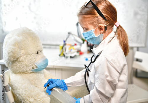Fototapeta Naklejka Na Ścianę i Meble -  a girl plays a doctor, listens, makes a virus test and a vaccination for a teddy bear