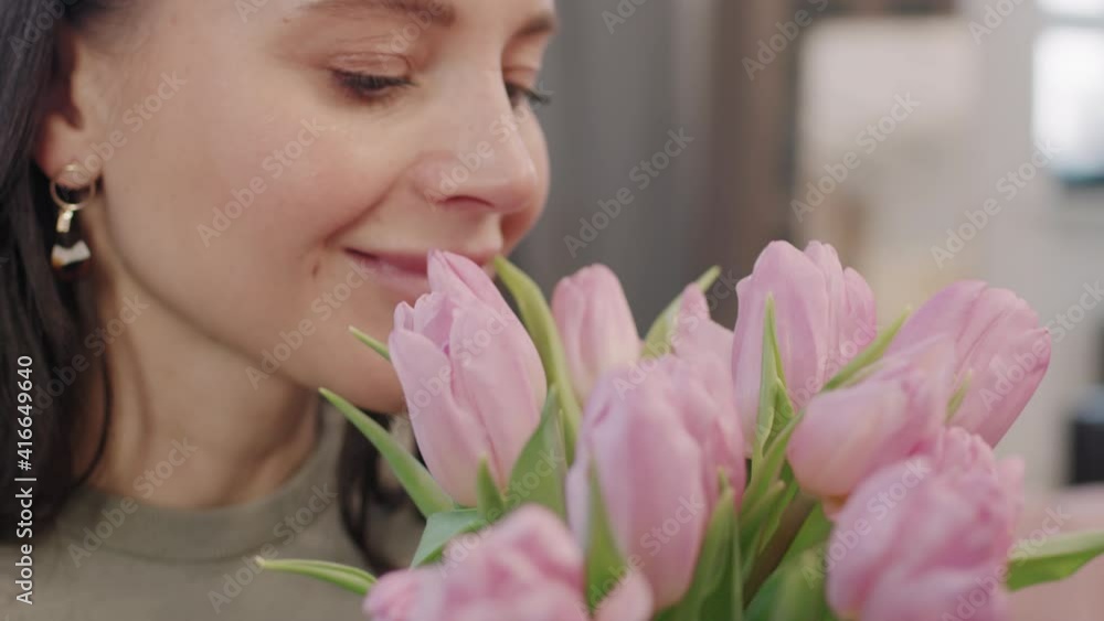 Slow-motion close up of attractive caucasian woman smiling while smelling scent of beautiful pink flowers Slow-motion close up of attractive caucasian woman smiling while smelling scent of beautiful pink flowers