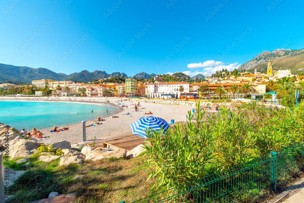 Tourists and locals enjoy a sunny day on the French Riviera as they relax on the sandy Plage de Fossan Mediterranean beach in Menton, France