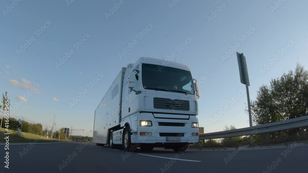 Cargo truck with cargo trailer driving on a highway. White Truck delivers goods in early hours of the Morning - very low angle drive thru close up shot. Cargo truck with cargo trailer driving on a highway. White Truck delivers goods in early hours of the Morning - very low angle drive thru close up shot.