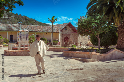 Peasant walks through the main park of Sora in Boyacá, Colombia with church in the background