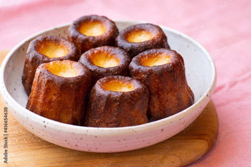 A close up of Canelés de Bordeaux on a white plate and pink table A close up of Canelés de Bordeaux on a white plate and pink table