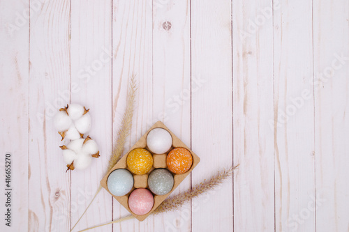 colorful eggs on white wooden background with the dry grass. Natural decor for Easter. 