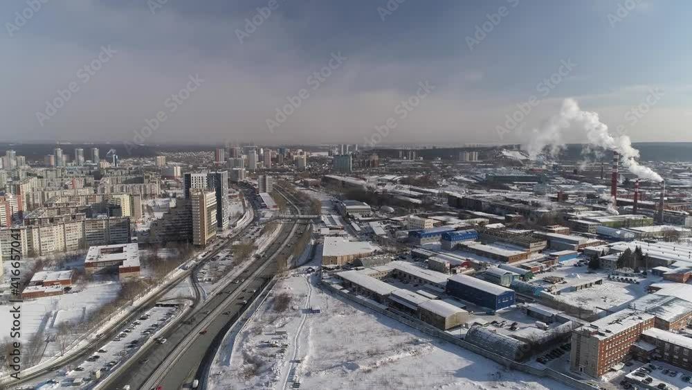 Aerial view of Highway with car traffic and Industrial Zone in the big city. Smoke (steam) is coming out of the chimneys. Nearby typical Soviet panel houses and modern multi-storey buildings. It's sno Aerial view of Highway with car traffic and Industrial Zone in the big city. Smoke (steam) is coming out of the chimneys. Nearby typical Soviet panel houses and modern multi-storey buildings. It's sno