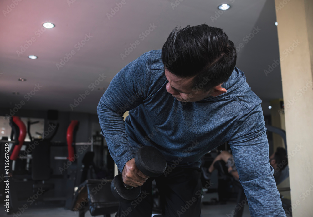 A focused asian man makes dumbbell triceps kickbacks on a bench at a