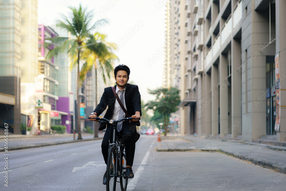 Asian businessman in a suit is riding a bicycle on the city streets for his morning commute to work. Eco Transportation Concept..