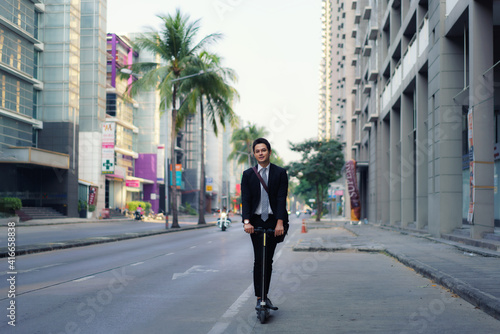 Asian businessman riding an electric scooter on the city streets to go to work in the morning. Daily commute that best reflect the working world of today. © ake1150