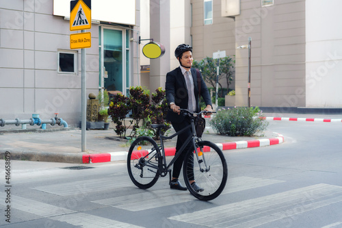 Asian businessman pushes a bicycle across a crosswalk on a city street during a morning commute.