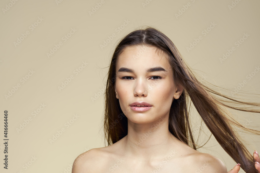 Brunette with bare shoulders close-up long hair beige background clean skin Brunette with bare shoulders close-up long hair beige background clean skin