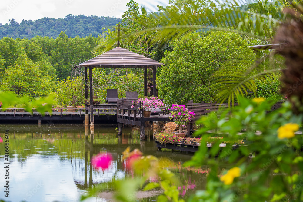 Wooden gazebo with sun loungers for relaxing on a terrace with flowers next to a lake on the tropical island of Thailand Wooden gazebo with sun loungers for relaxing on a terrace with flowers next to a lake on the tropical island of Thailand