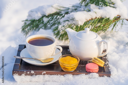 White cup of hot tea and teapot on a bed of snow and white background, close up