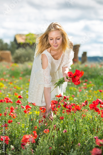 Beautiful young female in white dress holding bouquet of poppy flowers in fields