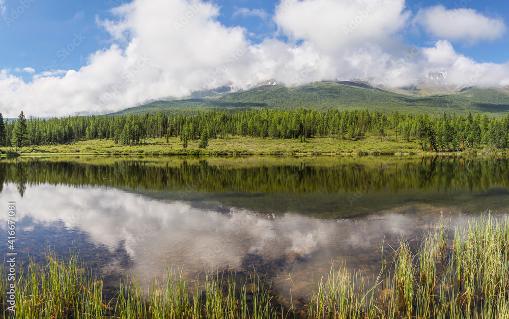 Forest lake on a quiet summer morning, clouds over mountain peaks	
