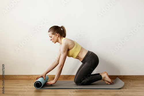 Fototapeta Naklejka Na Ścianę i Meble -  A young girl rolls out a yoga mat before taking a yoga class. Yoga, fitness, lifestyle