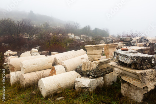 View of ancient sculptures fragments, reliefs and architectural elements outdoors on foggy winter day on archaeological site of Sagalassos in Turkey.. photo