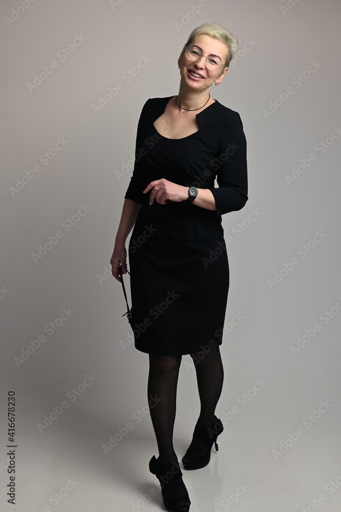 Full body portrait of business smiling caucasian woman with short hair wearing glasses and in a black business dress on a white background in the studio Full body portrait of business smiling caucasian woman with short hair wearing glasses and in a black business dress on a white background in the studio