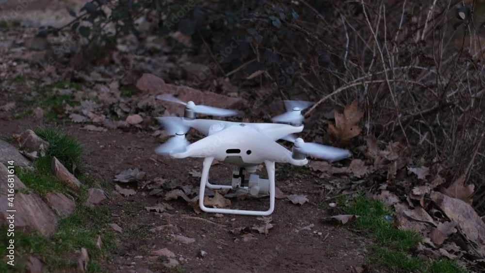 White RC quadcopter with digital camera taking off. Start the drone propellers. There are trees in the background and many dry autumn leaves moving around. Flying drone in nature concept close-up 4k White RC quadcopter with digital camera taking off. Start the drone propellers. There are trees in the background and many dry autumn leaves moving around. Flying drone in nature concept close-up 4k