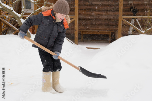 The boy cleans the snow with a shovel. It is snowing, small snowflakes all over the frame. © Sergei