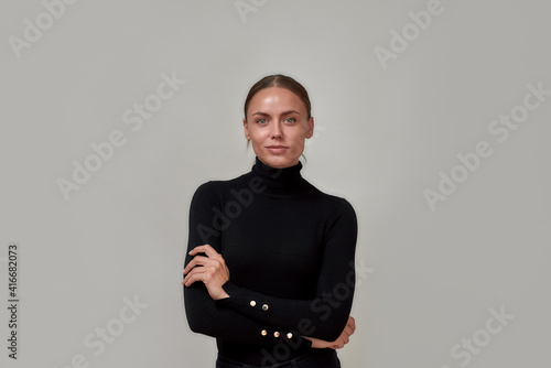 Portrait of beautiful caucasian woman wearing black turtleneck looking at camera, standing with arms crossed isolated over gray background