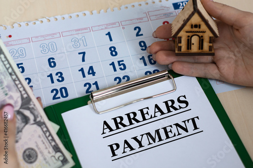 ARREARS PAYMENT - word in a folder against the background of women's hands with a house and money