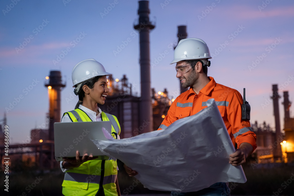 Fototapeta premium Two engineers working with laptop at front oil and gas refinery plant industry factory.