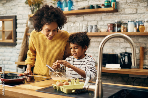 Happy black boy preparing food with his mother in the kitchen.