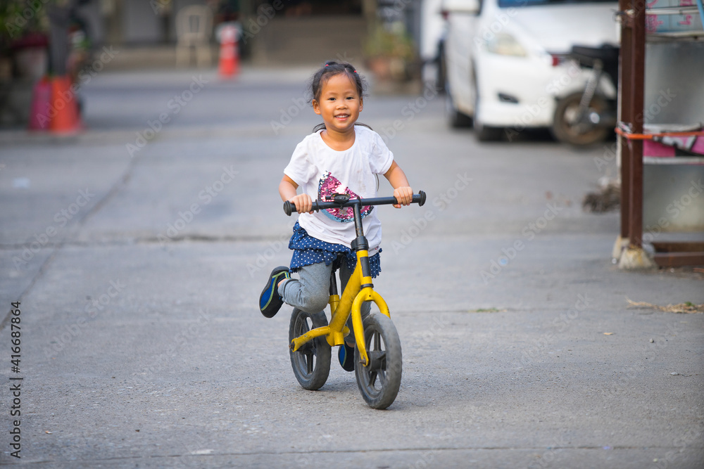 Asian Little girl learns to keep balance while riding a bicycle outdoors, active sport kids