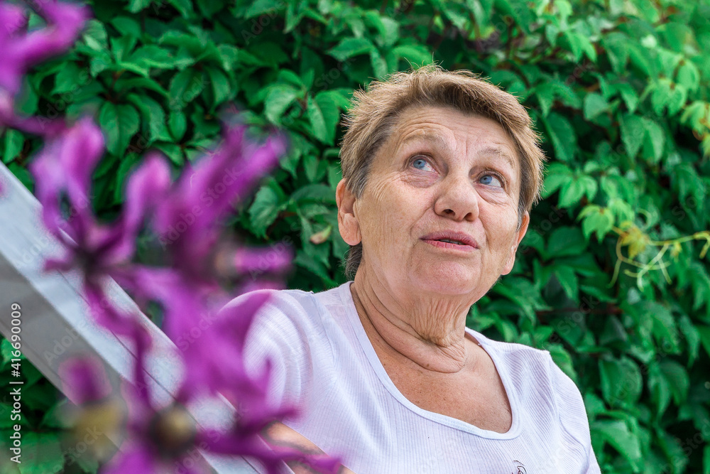 a woman of retirement age stands at her village house on the porch in summer in sunny weather and smiles a woman of retirement age stands at her village house on the porch in summer in sunny weather and smiles