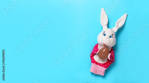 Banner with Easter bunny keeping the chocolate egg on blue background with copy space, empty text place. Christian holiday card. Online course learning of toy theater. Hand puppet. Design. Flat lay