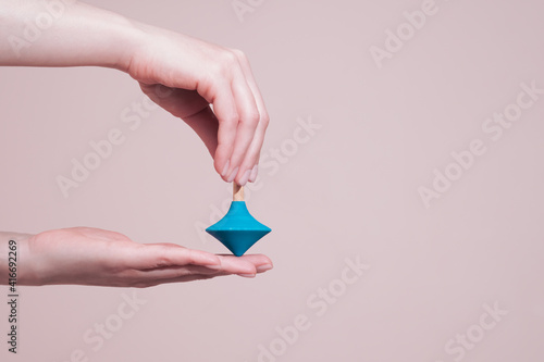 Female hands holding wooden whirligig or spinning top. Closeup, copy space. Balance and dynamic concept