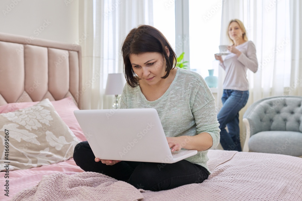 Serious mature woman with laptop at home, woman with cup background