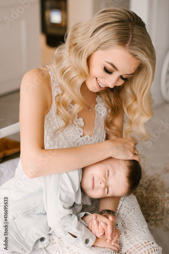 Beautiful young mother and son cuddle and play in smart clothes at home